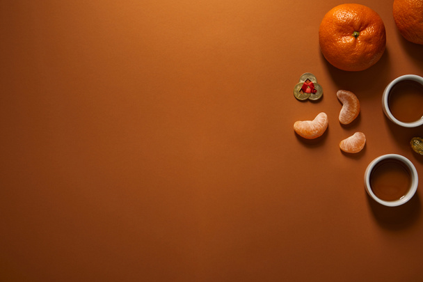 top view of fresh ripe tangerines, cups of tea and golden coins on brown background, chinese new year composition  - Fotografie, Obrázek