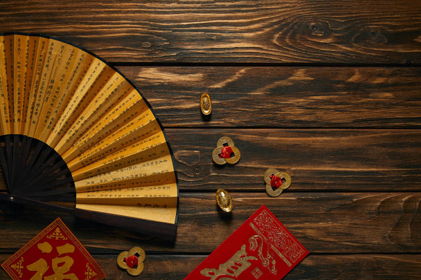 top view of fan with hieroglyphs and golden chinese decorations on wooden table  - Fotografie, Obrázek