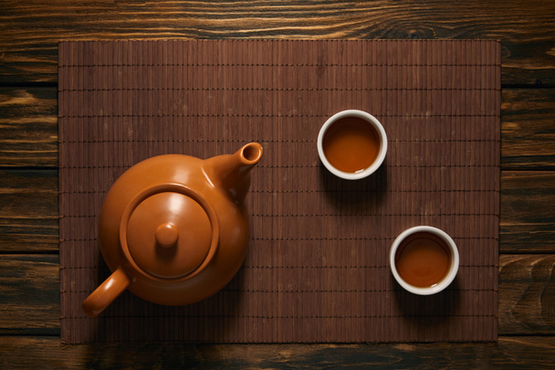 vista superior de la tetera de cerámica marrón y tazas de té en la estera de bambú
 - Foto, Imagen
