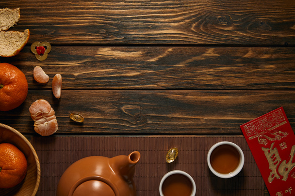 pohled shora z konvice, šálky čaje, čerstvé zralé mandarinky a tradiční čínské ozdoby na dřevěný stůl - Fotografie, Obrázek