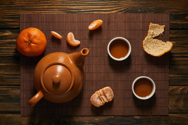 vista dall'alto di teiera, tazze di tè e mandarini su tappetino di bambù
 - Foto, immagini