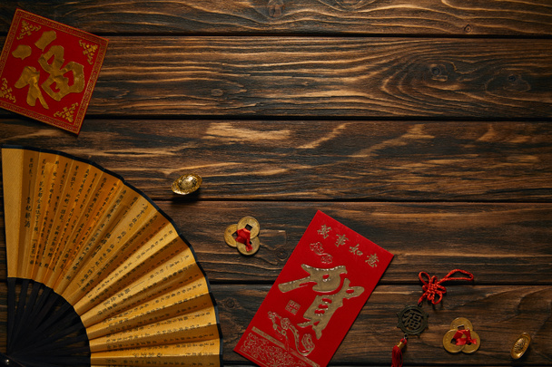 Chinees Nieuwjaar samenstelling met ventilator, hiërogliefen en decoratieve gouden munten op houten oppervlak (bovenaanzicht) - Foto, afbeelding