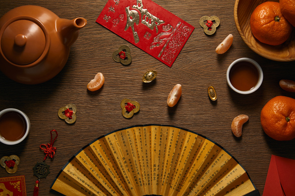 bovenaanzicht van verse rijpe mandarijnen, thee set, ventilator met hiërogliefen en gouden munten op houten tafel  - Foto, afbeelding