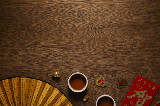vista superior de tazas de té, abanico con jeroglíficos y monedas de oro en la superficie de madera
 - Foto, imagen