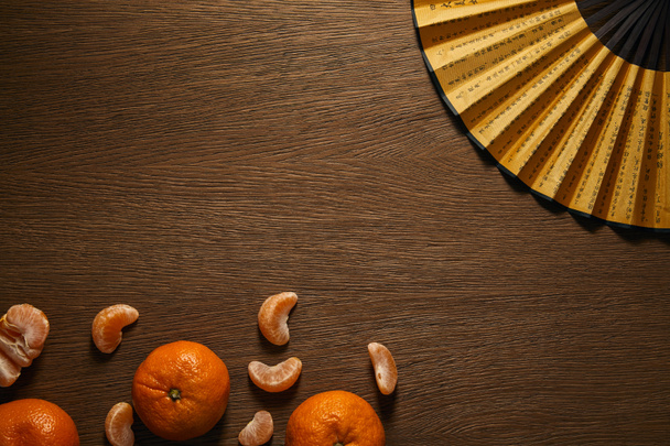 top view of fresh ripe tangerines and golden fan with hieroglyphs in wooden surface - Photo, Image