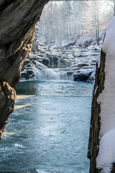 icy winter waterfall steaming between stones, orange sunlight, frozen pond - Photo, Image