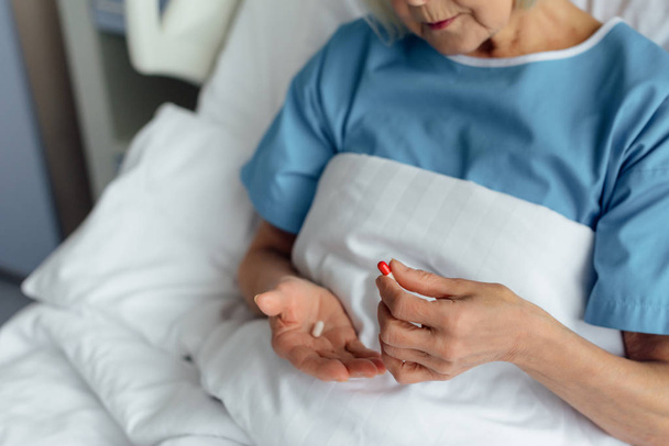 częściowy widok starszy Kobieta, leżąc w łóżku i przytrzymując pigułki w szpitalu - Zdjęcie, obraz