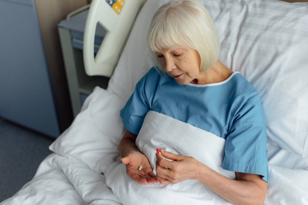 selective focus of senior woman lying in bed and holding pills in hospital - Photo, Image
