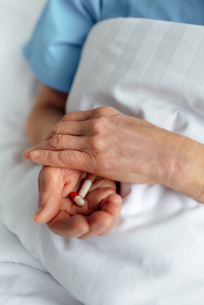 vista ritagliata di donna anziana sdraiata a letto e in possesso di pillole in ospedale
 - Foto, immagini