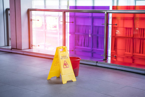 Señal de suelo húmedo de precaución amarilla en suelo húmedo con cubo rojo
 - Foto, imagen