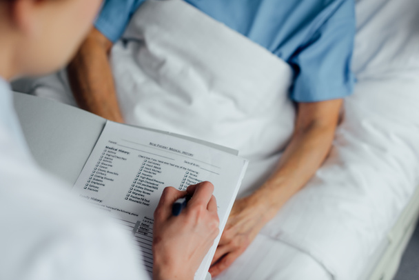 cropped view of doctor holding diagnosis and consulting woman lying in hospital bed  - Photo, Image