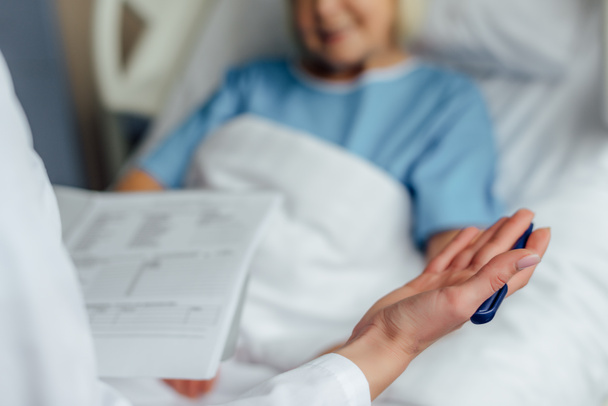 cropped view of doctor holding diagnosis and consulting patient lying in hospital bed  - Photo, Image