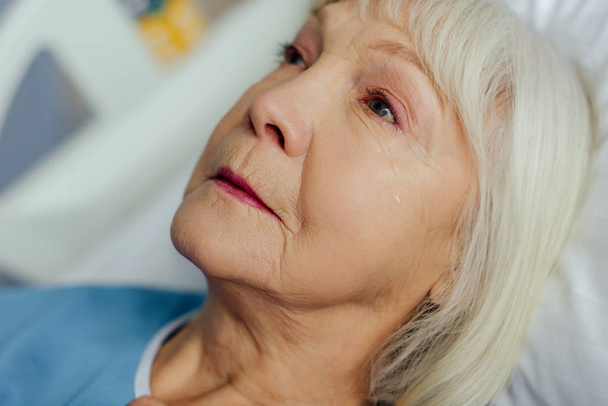 zbliżenie zdenerwowany starszy kobieta z siwymi włosami, leżąc w łóżku i płacz w szpitalu - Zdjęcie, obraz
