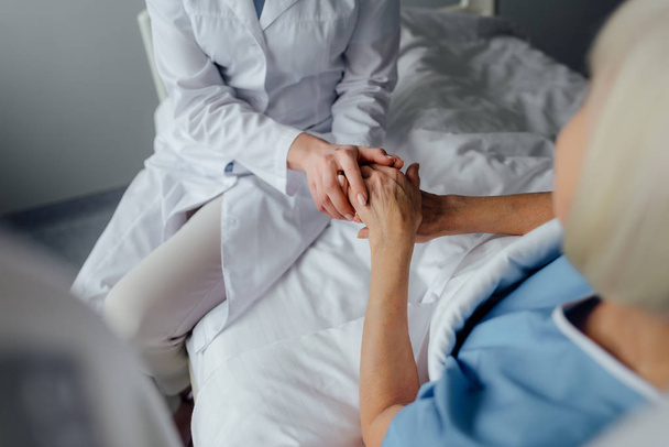 частковий вид на жінку-лікаря, який тримає руки з старшою жінкою, лежачи в ліжку в лікарні
 - Фото, зображення