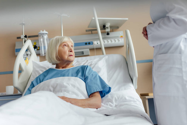 doctor consulting upset senior woman lying in hospital bed - Фото, зображення