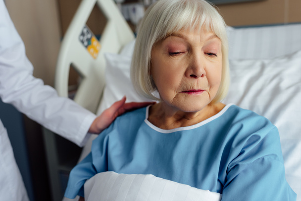 Ärztin tröstet verärgerte Seniorin mit grauen Haaren, die im Krankenhausbett liegt - Foto, Bild