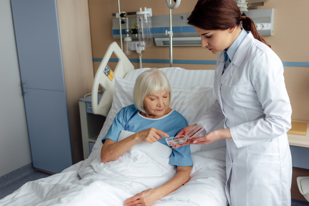 female doctor giving pills to senior woman lying in hospital bed - Фото, зображення