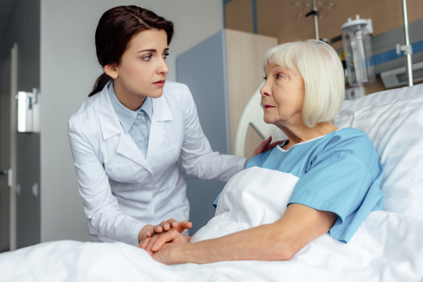 inquiet femme médecin tenant la main et consultant femme âgée couchée dans le lit d'hôpital
 - Photo, image