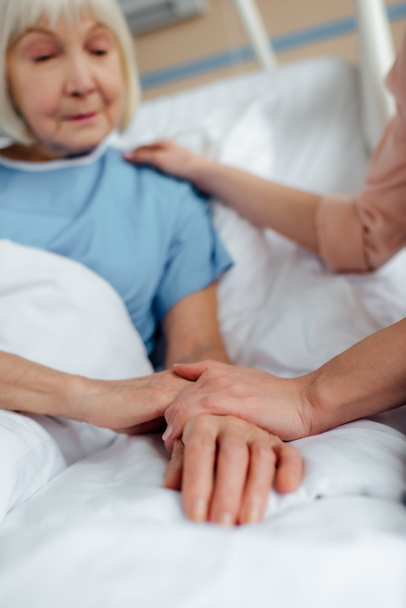 selective focus of senior woman and daughter holding hands in hospital - Foto, imagen