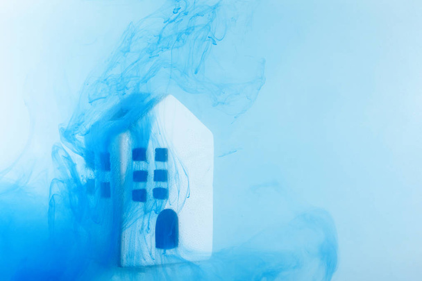 Small ceramic house under the water with blue acrylic paints. The concept of real estate, rent, sale or heating. White house from fairy tale. - Photo, Image