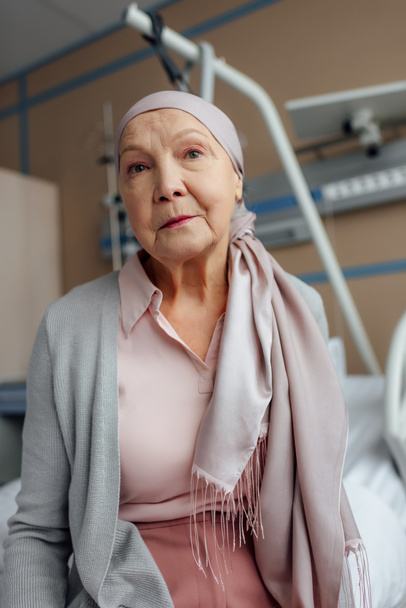 femme âgée en mouchoir avec cancer assis sur le lit à l'hôpital et regardant la caméra
 - Photo, image