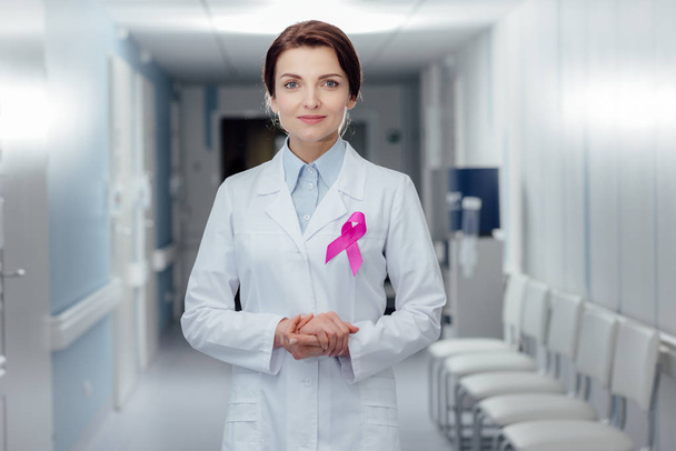 medico donna con nastro rosa e mani incrociate guardando la fotocamera in ospedale, concetto di consapevolezza del cancro al seno
 - Foto, immagini