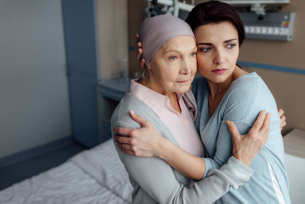 sad daughter embracing sick senior mother with cancer in hospital - Фото, изображение