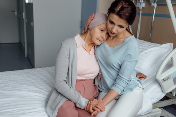 worried daughter hugging senior sad mother with cancer in hospital - Photo, Image