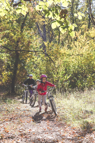 Мать и две дочери с велосипедами идут в гору в осеннем лесу
 - Фото, изображение