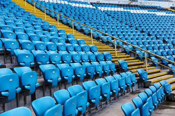 Άδειο παλιό πλαστικές καρέκλες στις κερκίδες του σταδίου. Πολλές κενές θέσεις για τους θεατές στις κερκίδες. Κενές πλαστικές καρέκλες, καθίσματα για τους οπαδούς του ποδοσφαίρου. Tribune, παιχνίδι χωρίς θεατές - Φωτογραφία, εικόνα
