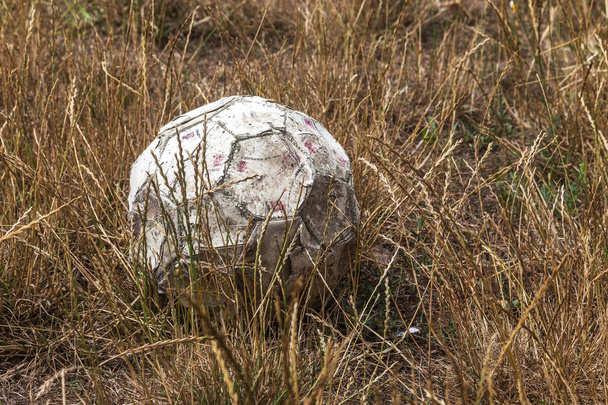 Staré opotřebované ošuntělý a roztrhané fotbalový míč na poli venkovské opuštěné stadionu. Třel, opotřebené, roztrhané s otvorem rozmazlený kožený míč na staré smetla drahýma stadionu. Staré kožené koule na trávě - Fotografie, Obrázek
