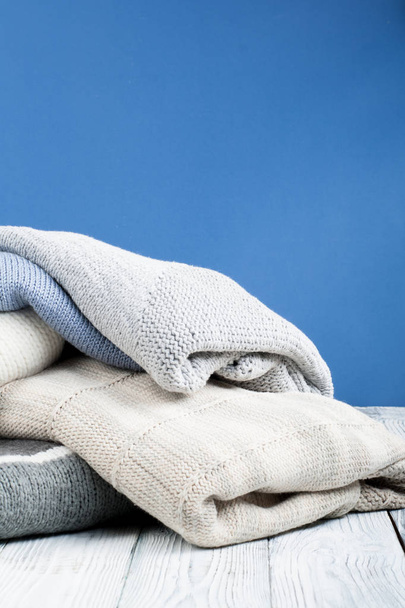 Knitted wool sweaters. Pile of knitted winter clothes on blue background - Fotografie, Obrázek