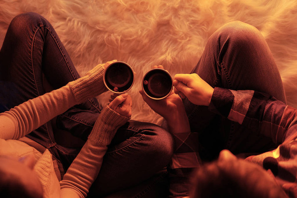 Crop top view of man and woman sitting in white furry rag having cups of warming drinks  - Photo, Image