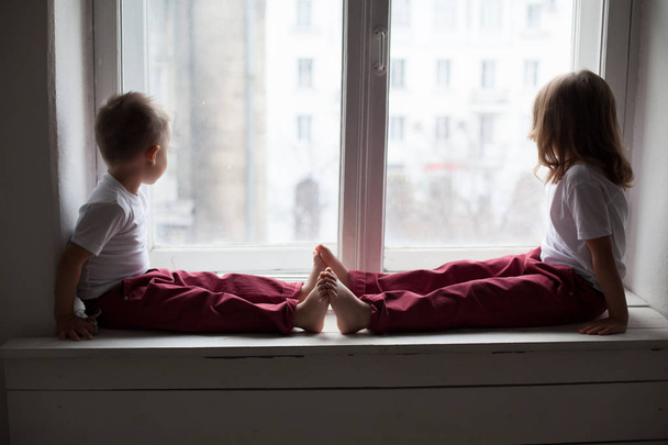 poika ja tyttö istuu ikkunalaudalla katsellen ulos ikkunasta
 - Valokuva, kuva