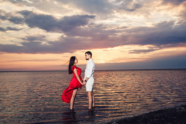 young couple in love holding hands in the sea against the backdrop of a beautiful sunset. - Photo, Image