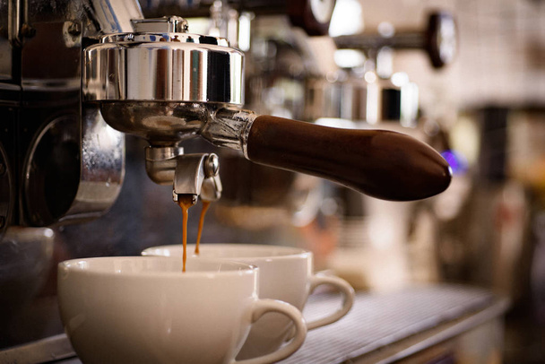 Twee kopjes koffie serveren op hetzelfde moment. Brouwen koffie met espressomachine. Koffie wordt gebrouwen in koffiehuis. Koffie bekers. Kleine bekers voor warme dranken. Espresso met portafilter maken - Foto, afbeelding