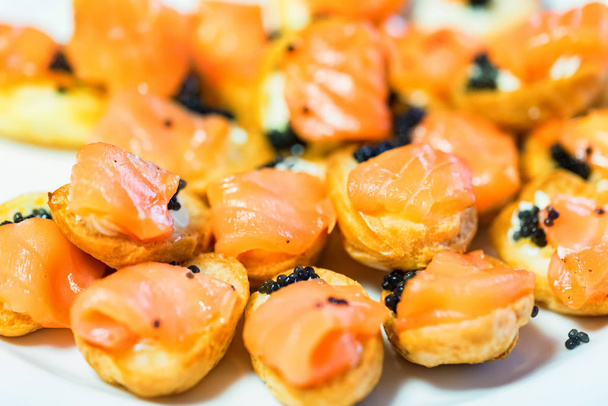 Вкусные профитроли с черной икрой и лососем на тарелке крупным планом
 - Фото, изображение