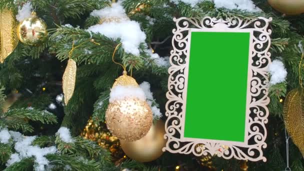 Gekrulde gesneden afbeeldingsframe opknoping op Fir Tree besprenkeld met sneeuw. Ingevoegde groene Chromakey in de witte Frame. Foto Frame Kerstmis en Nieuwjaar achtergrond, lege Mockuptemplate leeg. - Video