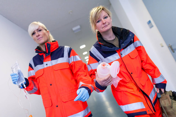 zwei weibliche Rettungssanitäter mit Notfallausrüstung in einer Etage - Foto, Bild