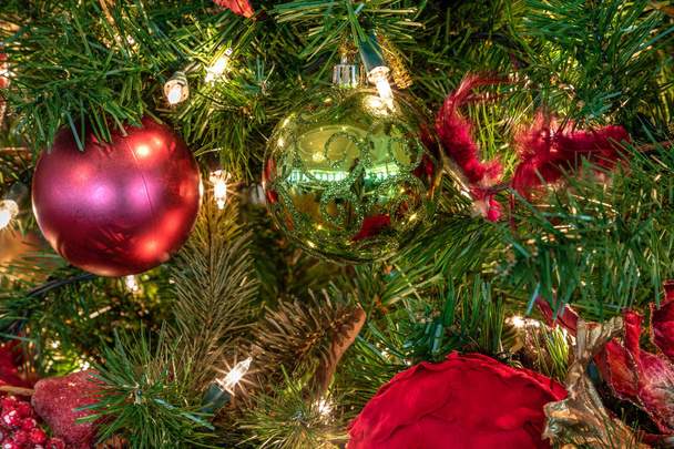 Ornamenti rossi e verdi su un albero di Natale con luci e fiocchi bianchi e decorazioni festive durante le festività natalizie
. - Foto, immagini