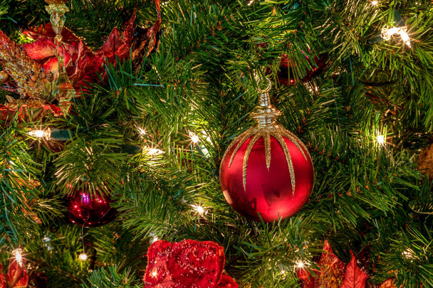 Красные и зеленые украшения на елке с белыми огнями и луками и праздничными украшениями вокруг праздничного сезона
. - Фото, изображение