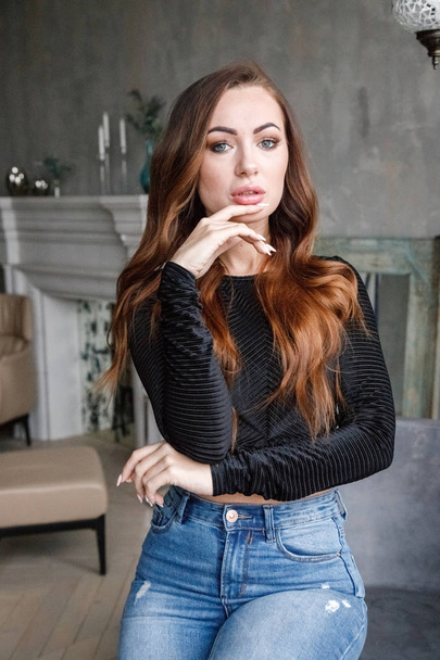 Portrait of beauty redhead woman in black blouse and blue jeans standing at luxury apartments interior   - Foto, Bild