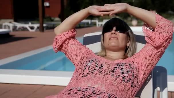 blond kobieta, leżąc na leżaku z obu rąk ukrywa jej twarz przed słońcem - Materiał filmowy, wideo