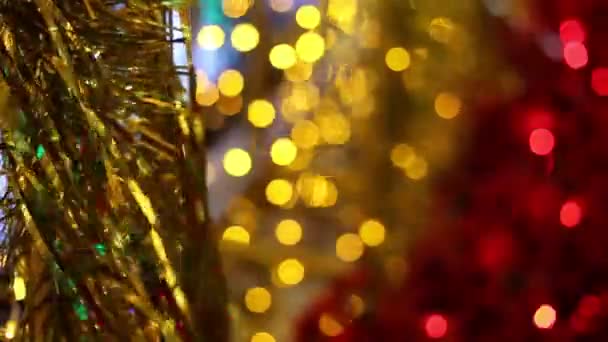 Celebración de Navidad y Año Nuevo. Adornos de guirnalda de oropel de Navidad de oro soplando en la brisa. Luces borrosas de Navidad parpadeando en el fondo
. - Imágenes, Vídeo