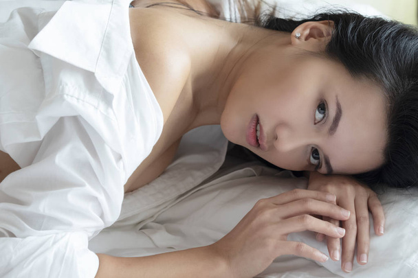 Beautiful Asian woman posing nude on a bed wearing a white shirt with white sheets - Foto, Imagen