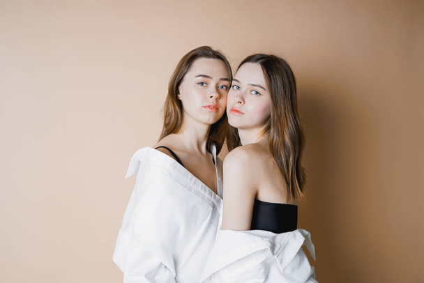 Módní modely dvě sestry dvojčata, krásné nahé dívky, při pohledu na fotoaparát izolované na béžové pozadí                                - Fotografie, Obrázek