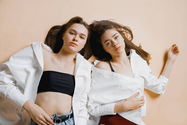 Mody modele dwie siostry bliźniaczki piękne dziewczyny nago, patrząc na kamery na białym tle na beżowym tle                                - Zdjęcie, obraz
