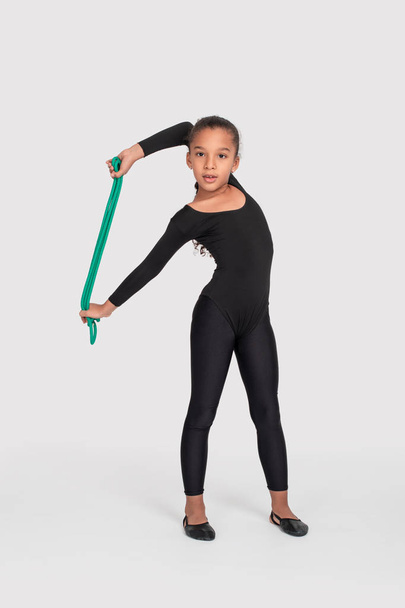 Studio shot of   attractive little  gymnast girl of mulatta with long braid of frizzy wearing  black legends and a bathing suit with a green jump rope on a white background, full length.   - Foto, afbeelding