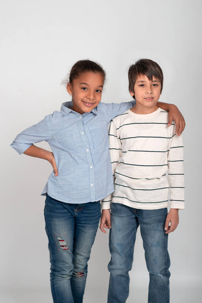 Foto de estudio de dos amigos, niño y niña, con jeans y camisetas. Chica sonriendo con su mano en el hombro del chico
. - Foto, imagen