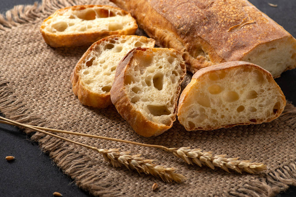 スライスされたジュート ナプキンをテーブルの上に嘘を小麦の耳と伝統的なチャバタのパン。次に、ナイフは、します。 - 写真・画像